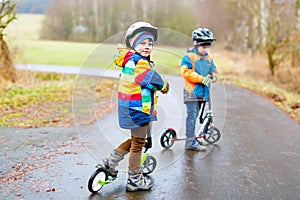 Two little kid boys, best friends riding on scooter in park