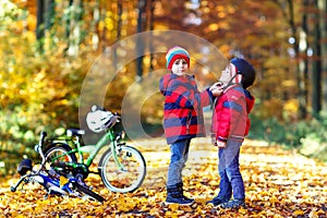 Two little kid boys with bicycles in autumn forest putting helmets