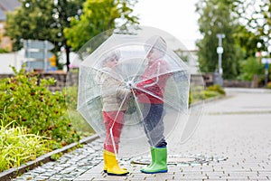 Two little kid boys with big umbrella outdoors