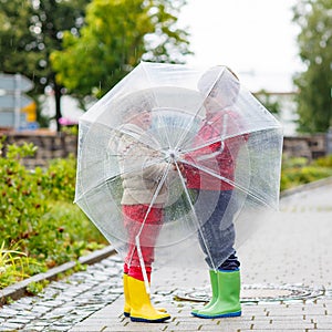 Two little kid boys with big umbrella outdoors