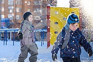 Two little kid boys in colorful clothes playing outdoors during snowfall. Active leisure with children in winter on cold days. Hap