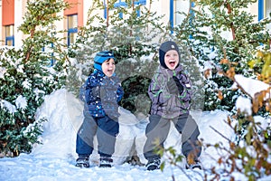 Two little kid boys in colorful clothes playing outdoors during snowfall. Active leisure with children in winter on cold days. Hap