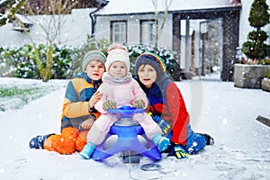 Two little kid boys and cute toddler girl sitting together on sledge. Siblings, brothers and baby sister enjoying sleigh