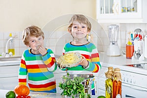 Two little kid boys eating spaghetti in domestic kitchen.