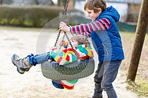 Two little kid boys having fun with chain swing on outdoor playground. Children, best friends and siblings swinging on