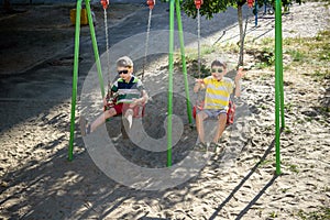 Two little kid boys having fun with swing on outdoor playground