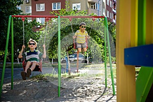 Two little kid boys having fun with swing on outdoor playground