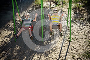 Two little kid boys having fun with swing on outdoor playground