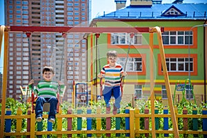 Two little kid boys having fun with swing on outdoor playground. Children, best friends and siblings swinging on warm sunny spring