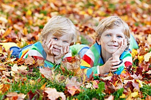 Two little kid boys laying in autumn leaves in colorful clothing