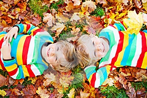 Two little kid boys laying in autumn leaves in colorful clothing