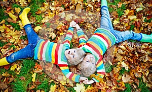 Two little kid boys laying in autumn leaves in colorful clothing