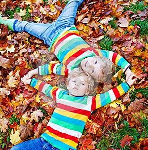 Two little kid boys laying in autumn leaves in colorful clothing