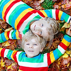 Two little kid boys laying in autumn leaves in colorful clothing