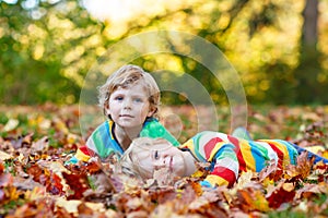 Two little kid boys laying in autumn leaves in colorful clothing