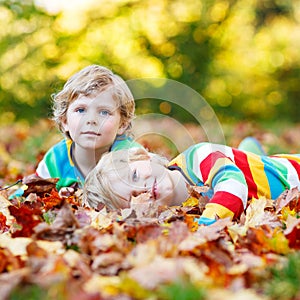 Two little kid boys laying in autumn leaves in colorful clothing