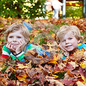 Two little kid boys laying in autumn leaves in colorful clothing