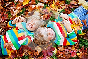 Two little kid boys laying in autumn leaves in colorful clothing