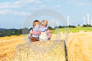 Two little kid boys, twins and siblings sitting on warm summer day on hay stack in wheat field. Happy children playing