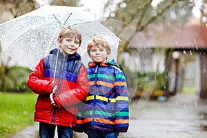 Two little kid boys on way to school walking during sleet, rain and snow with umbrella on cold day. Children, best
