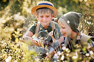 Two little kids with backpacks examining plants through magnifying glass in forest