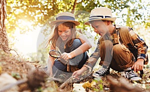 Two little kids with backpacks examining plants through magnifying glass in forest