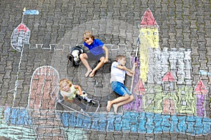 Two little kids boys and cute toddler girl drawing knight castle with colorful chalks on asphalt. Happy siblings and