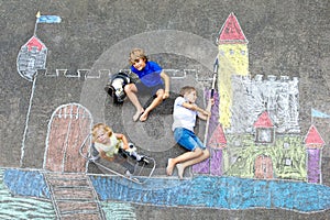 Two little kids boys and cute toddler girl drawing knight castle with colorful chalks on asphalt. Happy siblings and