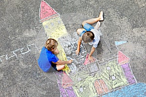 Two little kids boys drawing knight castle with colorful chalks on asphalt. Happy siblings and friends having fun with