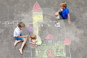 Two little kids boys drawing knight castle with colorful chalks on asphalt. Happy siblings and friends having fun with