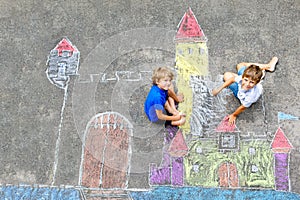 Two little kids boys drawing knight castle with colorful chalks on asphalt. Happy siblings and friends having fun with