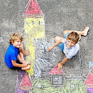 Two little kids boys drawing knight castle with colorful chalks on asphalt. Happy siblings and friends having fun with