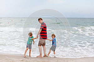 Two little kids boys and father on the beach of ocean