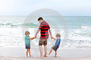 Two little kids boys and father on the beach of ocean