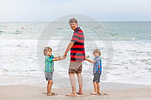 Two little kids boys and father on the beach of ocean