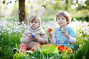 Two little kids boys and friends in Easter bunny ears during traditional egg hunt in spring garden, outdoors. Siblings