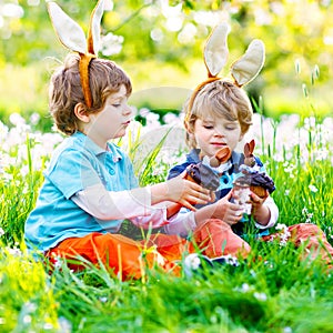 Two little kids boys and friends in Easter bunny ears during traditional egg hunt in spring garden, outdoors. Siblings