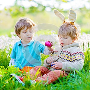 Two little kids boys and friends in Easter bunny ears during traditional egg hunt in spring garden, outdoors. Siblings
