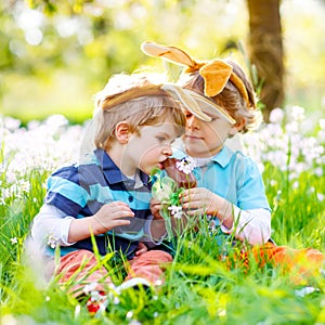 Two little kids boys and friends in Easter bunny ears during traditional egg hunt in spring garden, outdoors. Siblings