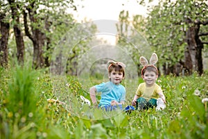 Two little kids boys and friends in Easter bunny ears during traditional egg hunt in spring garden, outdoors. Siblings having fun