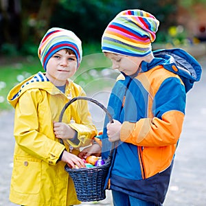 Two little kids boys and friends making traditional Easter egg hunt in spring garden, outdoors. Siblings having fun with