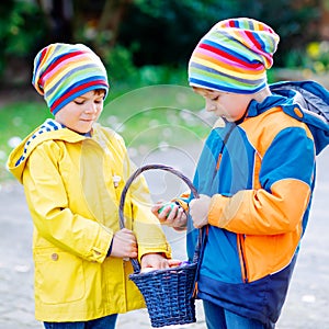 Two little kids boys and friends making traditional Easter egg hunt in spring garden, outdoors. Siblings having fun with