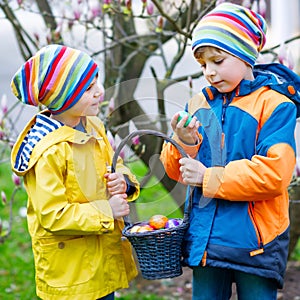 Two little kids boys and friends making traditional Easter egg hunt in spring garden, outdoors. Siblings having fun with