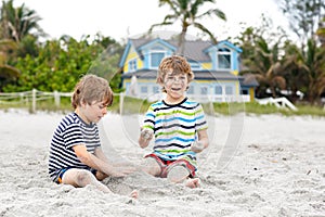 Two little kids boys having fun with building sand castle on tropical beach