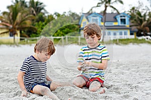 Two little kids boys having fun with building sand castle on tropical beach