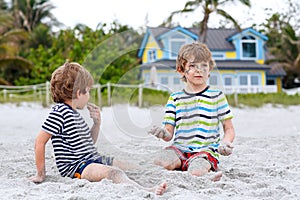 Two little kids boys having fun with building sand castle on tropical beach
