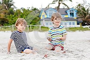 Two little kids boys having fun with building sand castle on tropical beach