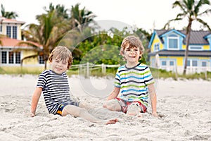 Two little kids boys having fun with building sand castle on tropical beach