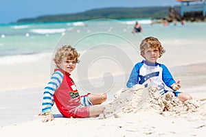 Two little kids boys having fun with building a sand castle on tropical beach of carribean island.