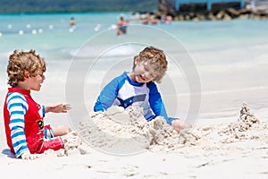 Two little kids boys having fun with building a sand castle on tropical beach of carribean island.